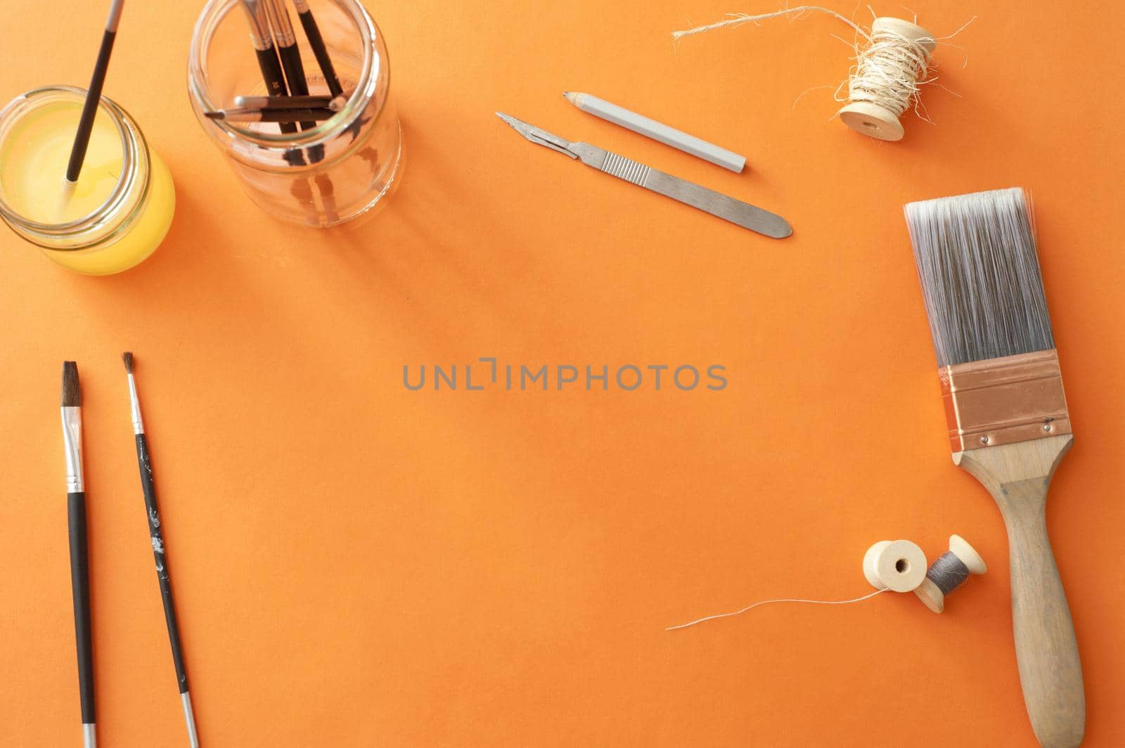 High Angle Still Life of Various Art Supplies and Paintbrushes Scattered on Orange Surface with Copy Space in Center of Page