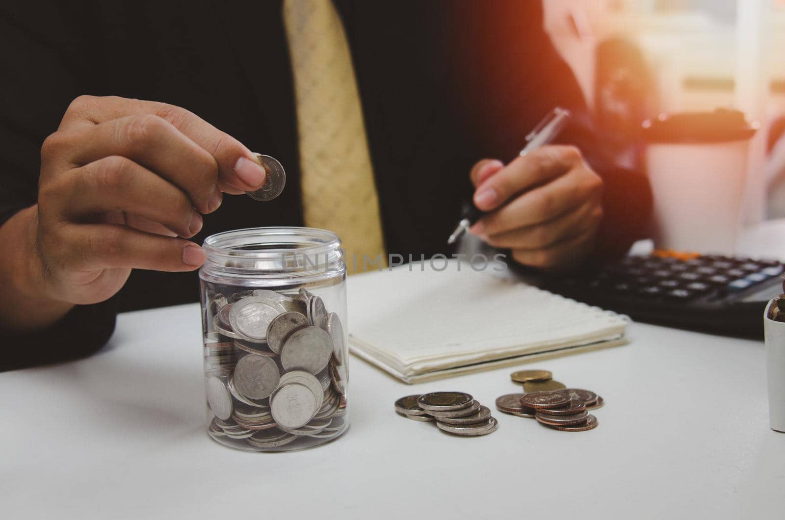 Man hand putting money coin and take note of income and expenses and working to save money for the future growing business, education and retirement.