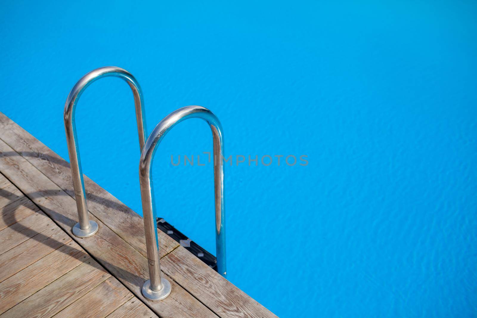 Ladder stainless handrails for descent into swimming pool. Swimming pool with handrail . Ladder of a swimming pool. People swim and relax in the pool