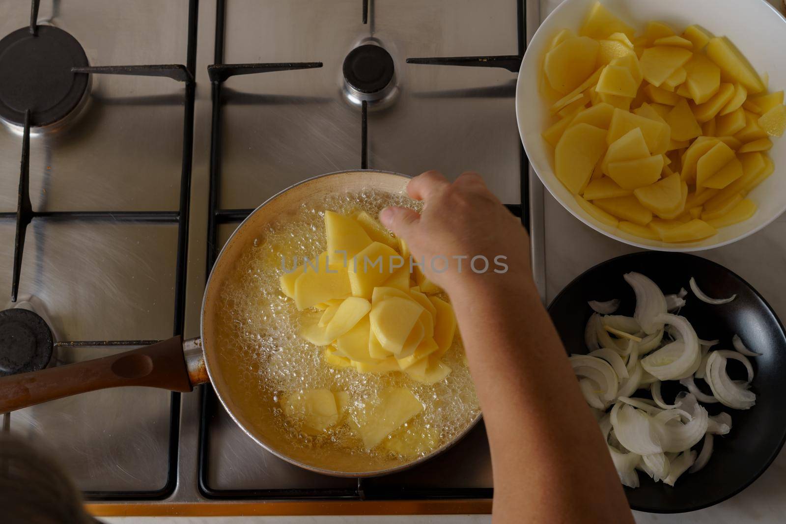top view of a woman's arm dropping potatoes into boiling oil to make a potato omelet