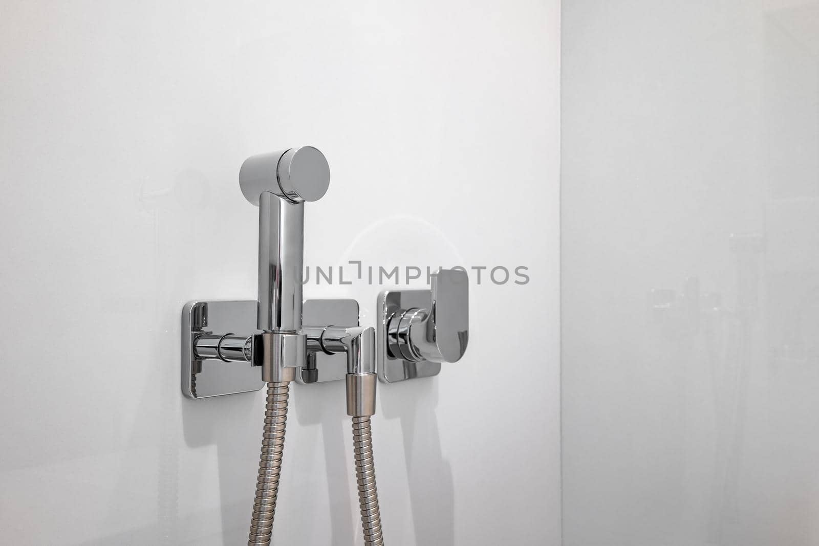 Chromium bidet shower with white tiles in a toilet. Silver bidet spray shower
