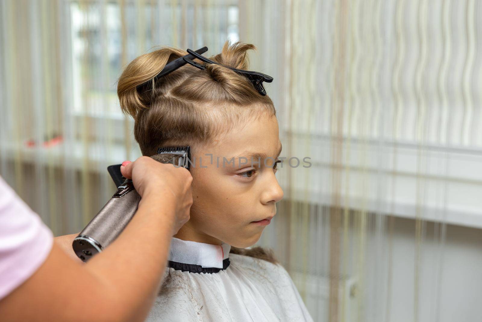 Nice european boy getting hairstyle in barbershop. Hairdresser makes a hairstyle for a boy.