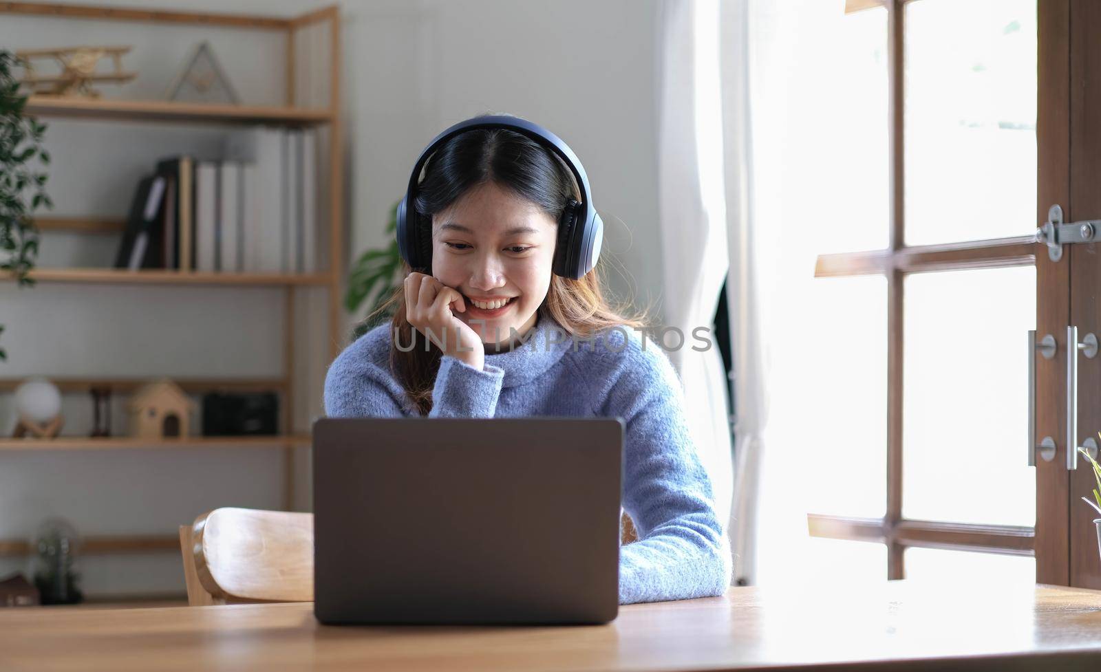 Cheerful beautiful Asian woman wearing headphones and look to digital tablet at video calling meeting and study online on the Internet..