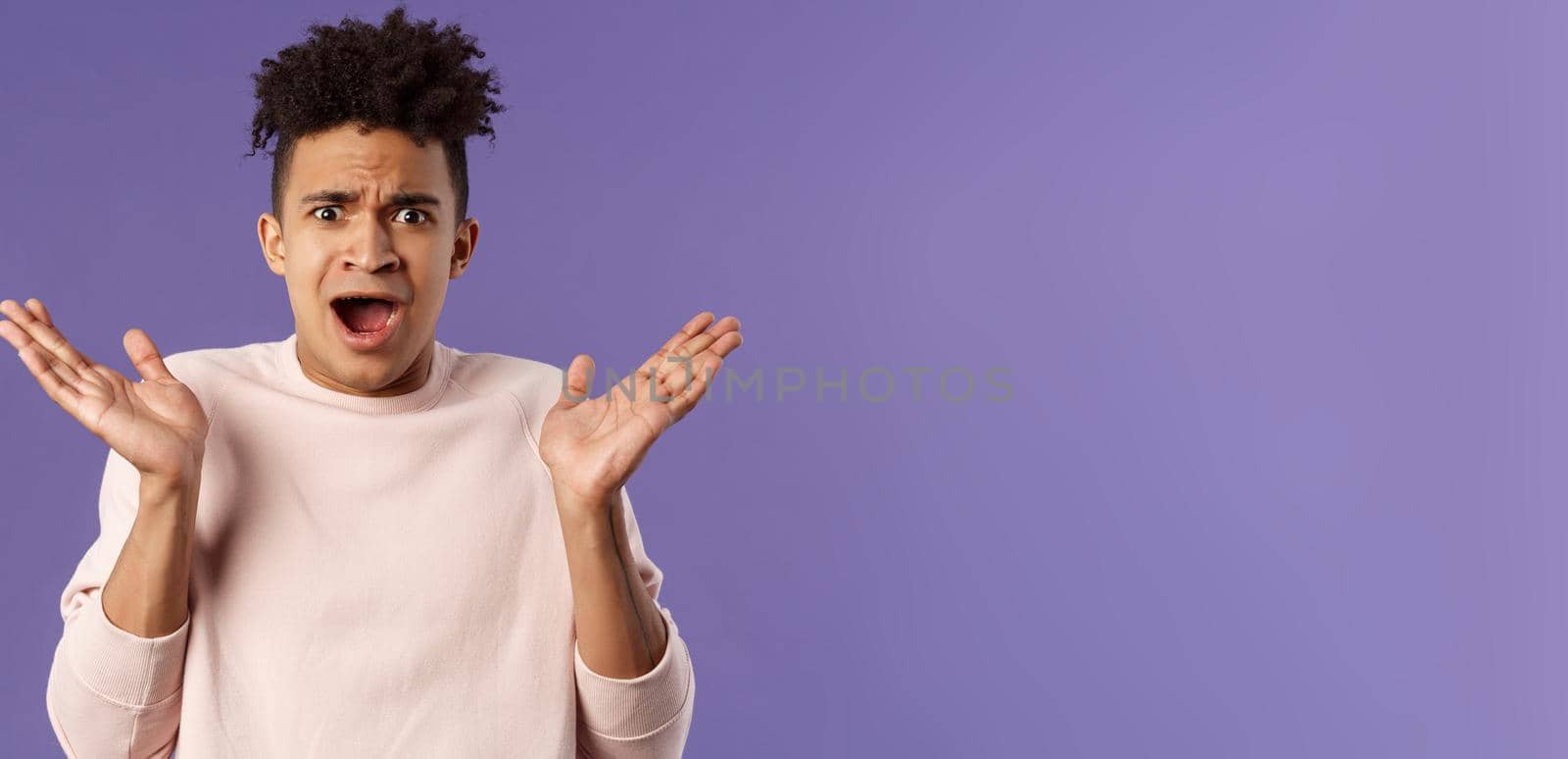 Close-up portrait of displeased, bothered frustrated hispanic man spread hands sideways in dismay and confusion, staring camera upset with disappointed grimacing expression, purple background.