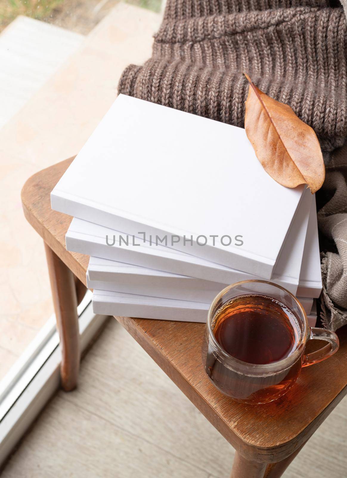 Stack of white blank books with autumn leaves and cup of hot tea on old wooden chair, mockup design by Desperada
