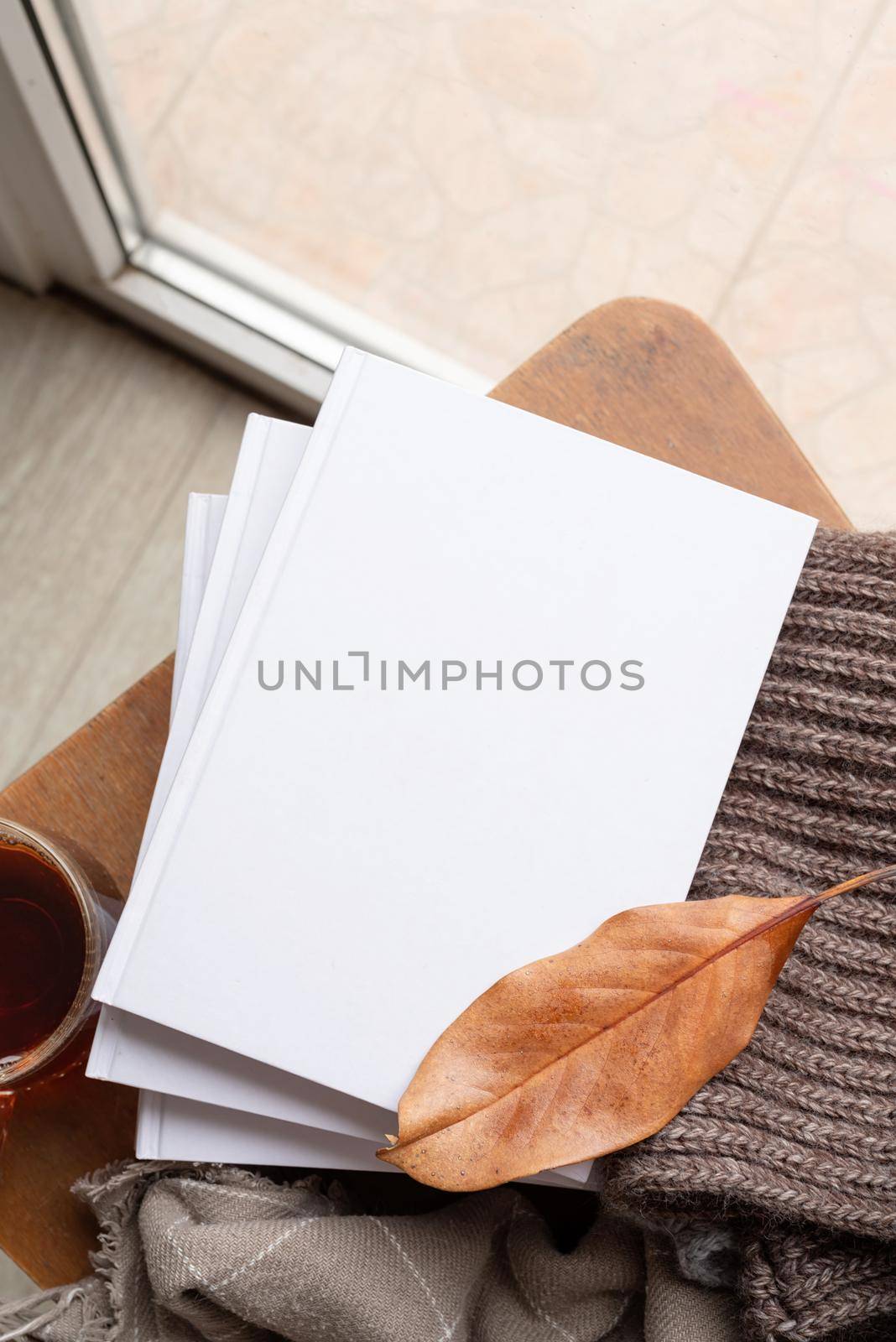 Stack of white blank books with autumn leaves and cup of hot tea on old wooden chair, mockup design by Desperada