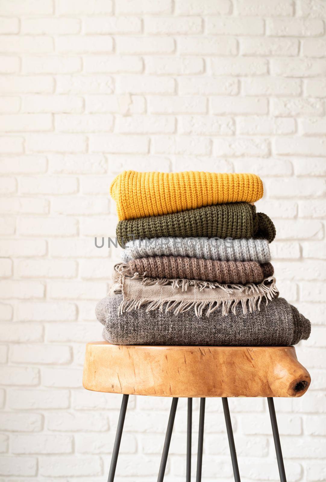 Hello fall. Cozy warm image. Stack of autumn warm sweaters on modern coffee table, white brick wall background