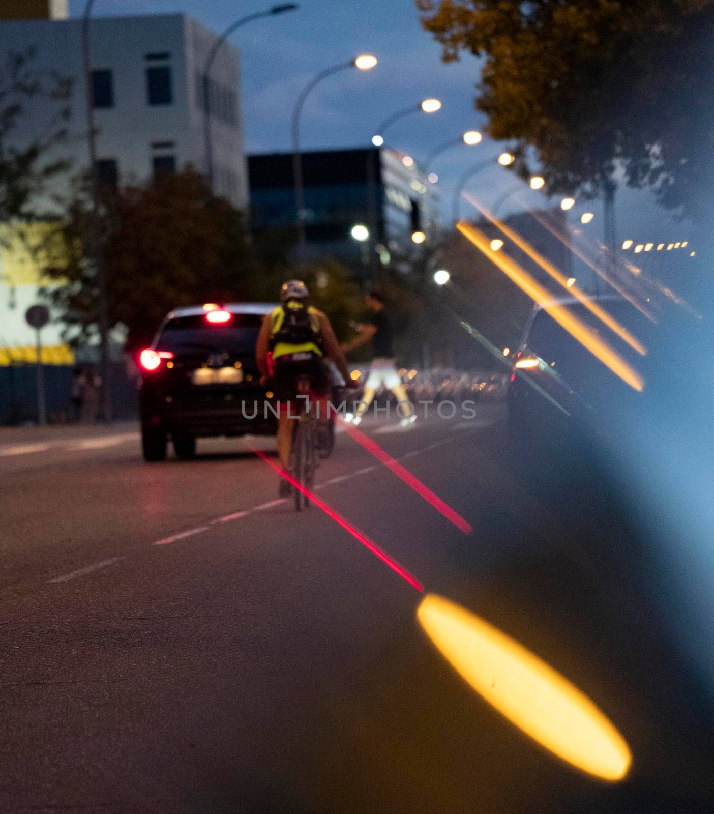 defocused night lights reflections. car and biker stopping as pedestrian is crossing the road.