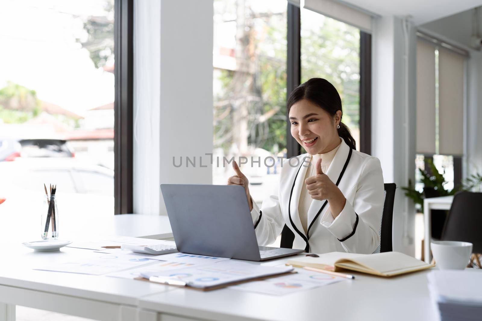 Asian business woman thumbs up to her colleagues about plan in video conference. Multiethnic business team using computer for a online meeting in video call. by nateemee