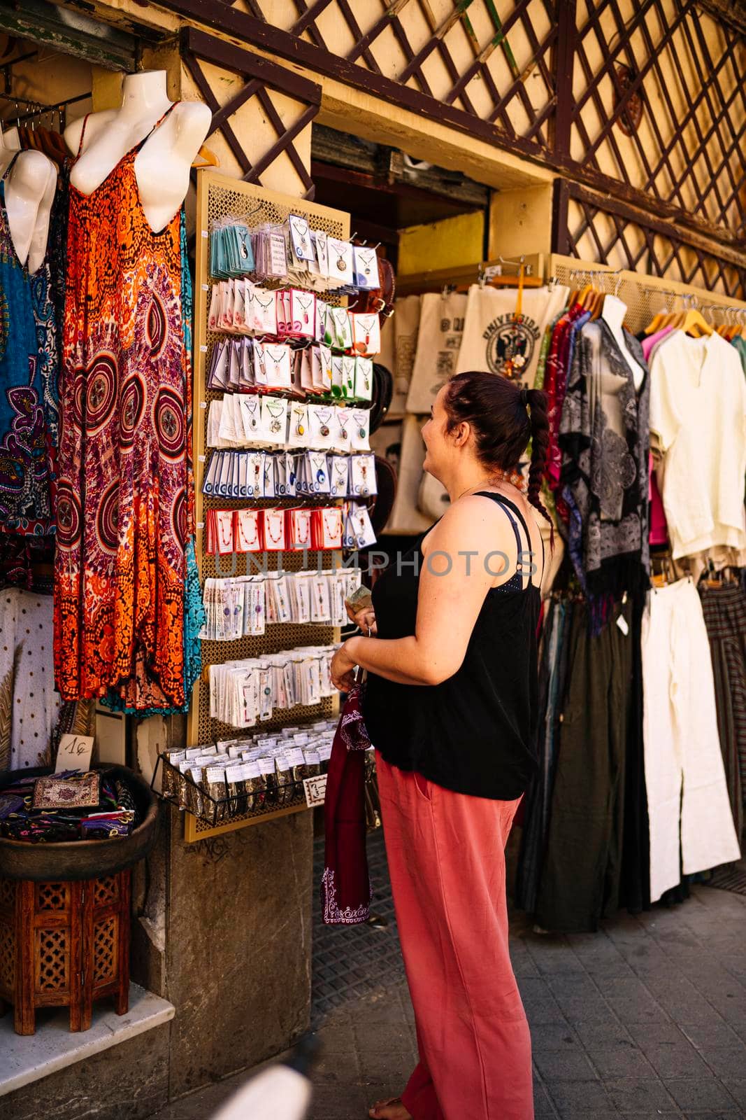 Happy female tourist smiling and looking at camera while choosing accessories on rack on clothes market