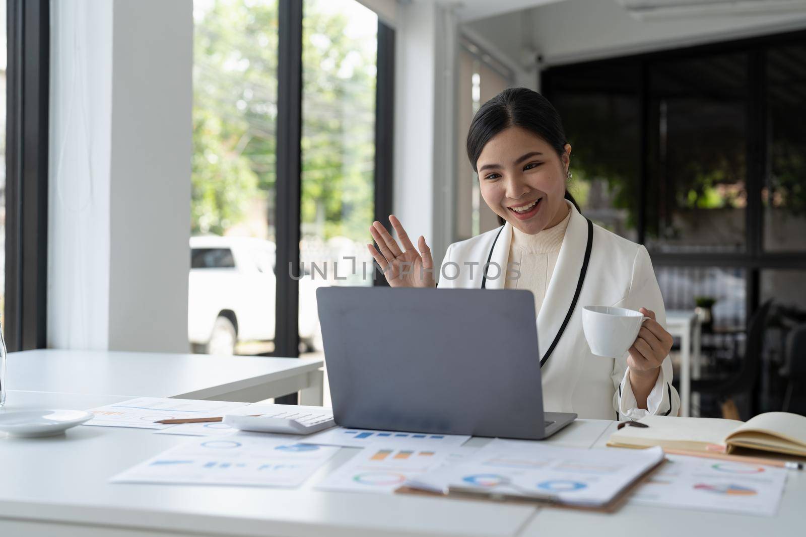 Asian woman holding webinar or giving online business consultation to client. Female entrepreneur or corporate company manager having remote online telework meeting via video call on laptop computer by nateemee