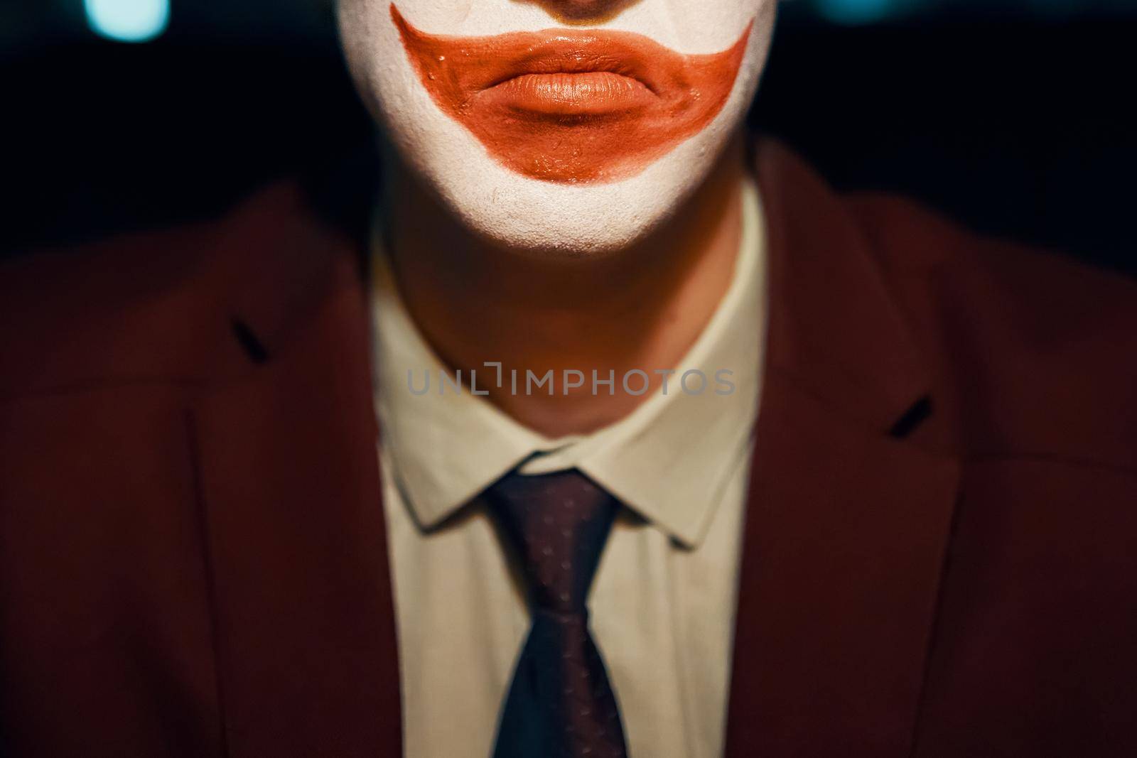Close-up of a guy's mouth with joker makeup. Man in a suit and tie. Halloween party.