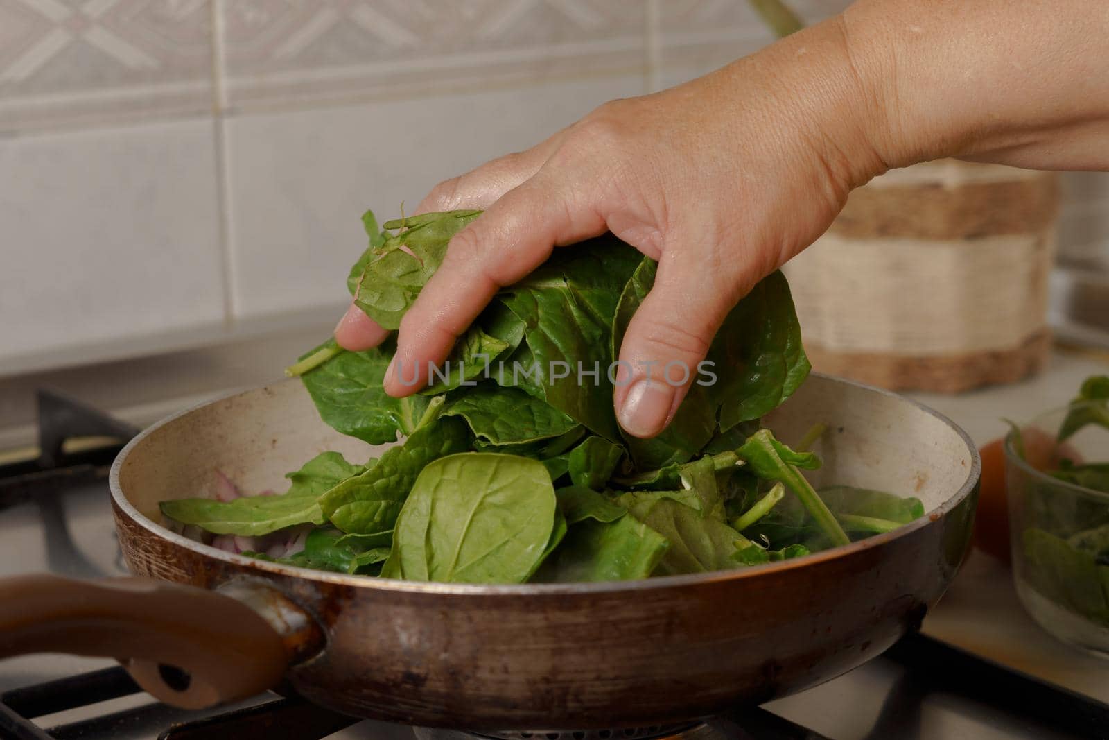 close-up of a woman's hand throwing spinach into a frying pan on her kitchen stove