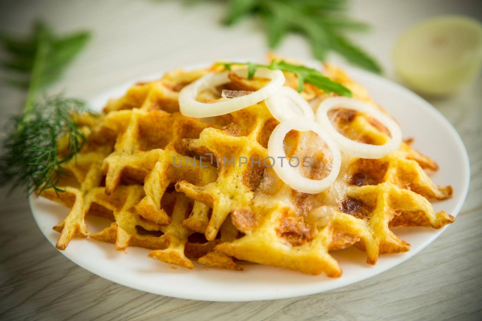 fried potato cheese vegetable waffles with bacon and onions in a plate, on a wooden table.