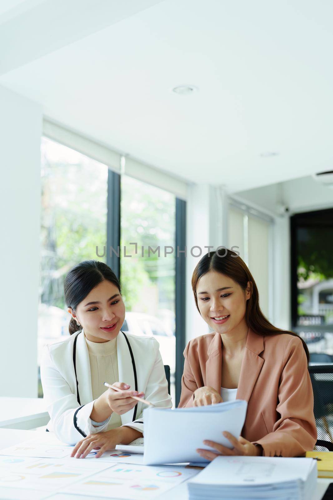 two asian businesswoman using documents to analyze jobs. by Manastrong