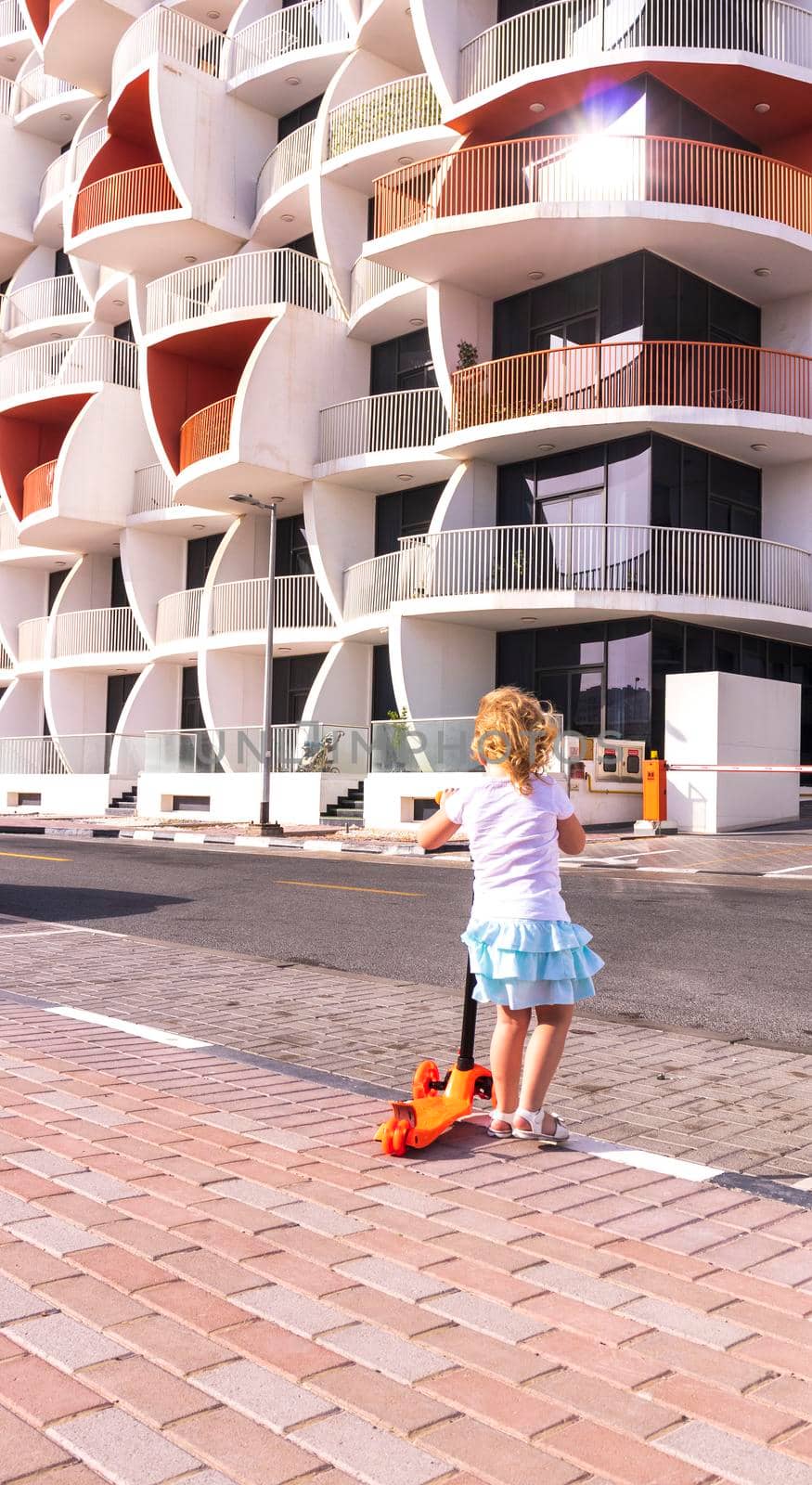 Dubai, UAE - 04.02.2021 - Little girl riding a scooter in front of Binghatti pearls residential building.