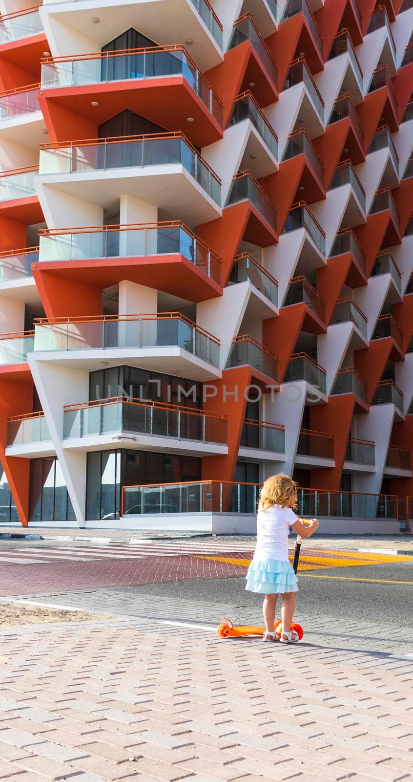 Dubai, UAE - 04.02.2021 - Little girl riding a scooter in front of Binghatti crystals residential building.