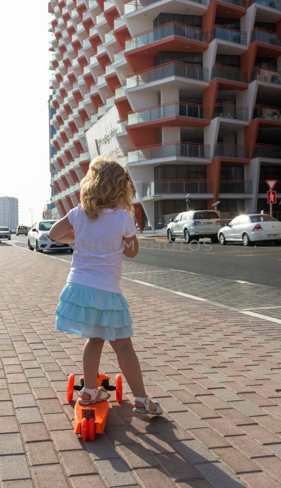 Dubai, UAE - 04.02.2021 - Little girl riding a scooter in front of Binghatti crystals residential building.