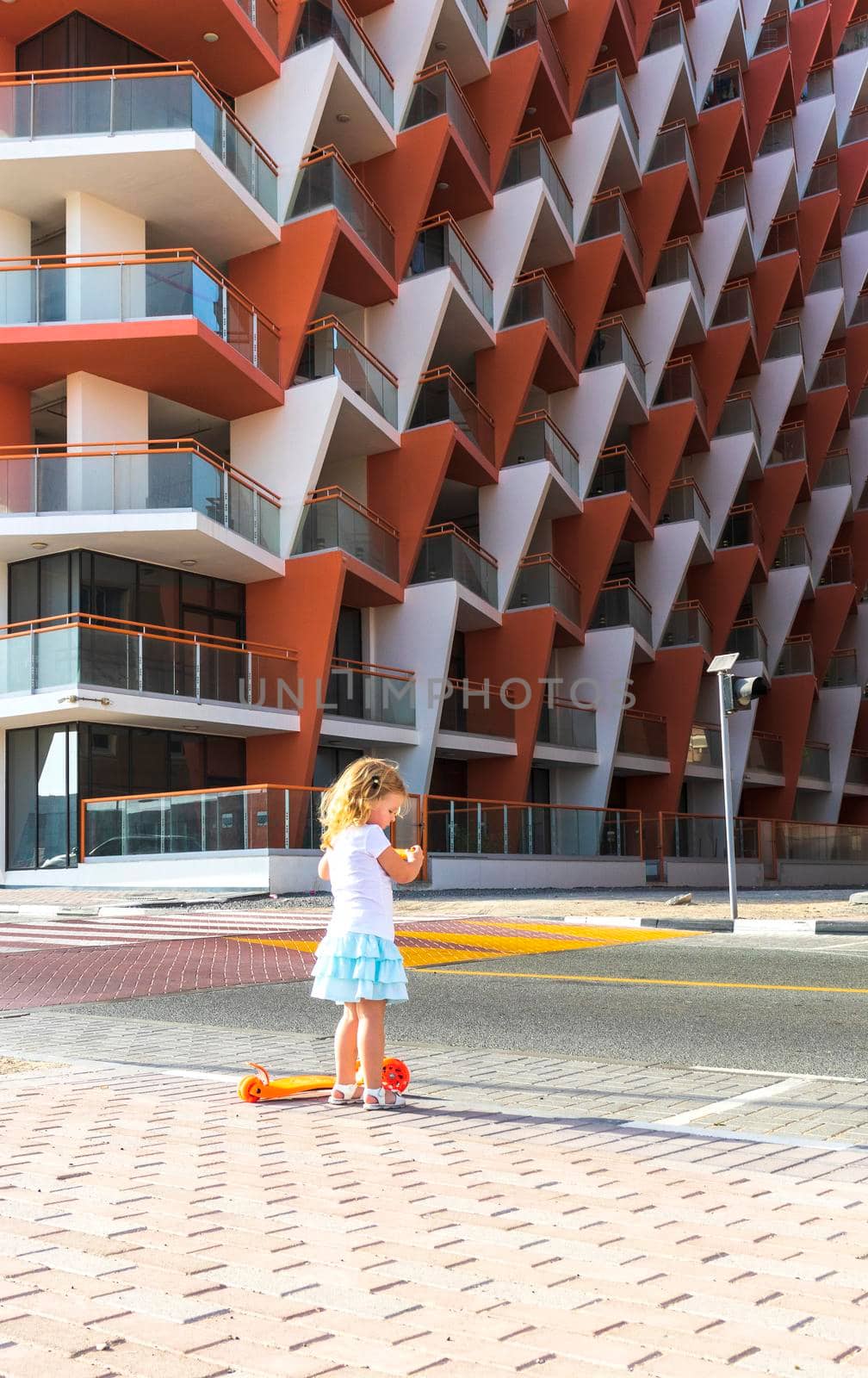 Dubai, UAE - 04.02.2021 - Little girl riding a scooter in front of Binghatti crystals residential building.