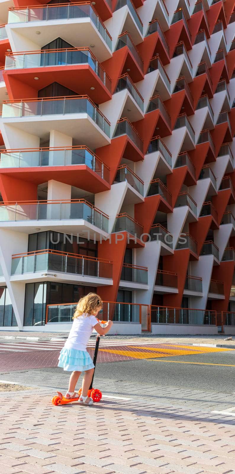 Dubai, UAE - 04.02.2021 - Little girl riding a scooter in front of Binghatti crystals residential building.