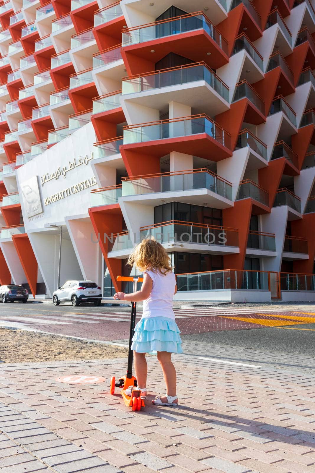 Dubai, UAE - 04.02.2021 - Little girl riding a scooter in front of Binghatti crystals residential building.