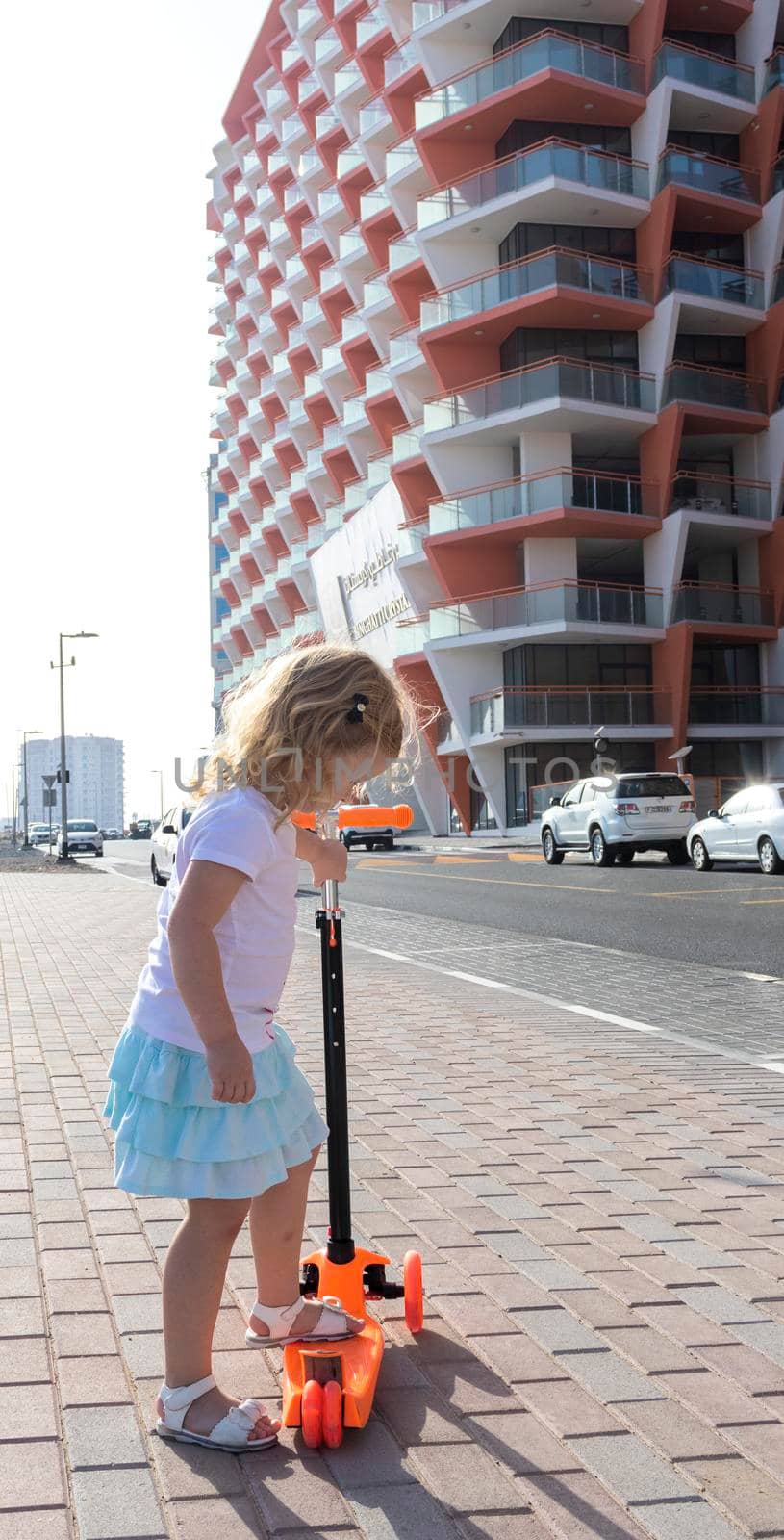Dubai, UAE - 04.02.2021 - Little girl riding a scooter in front of Binghatti crystals residential building.