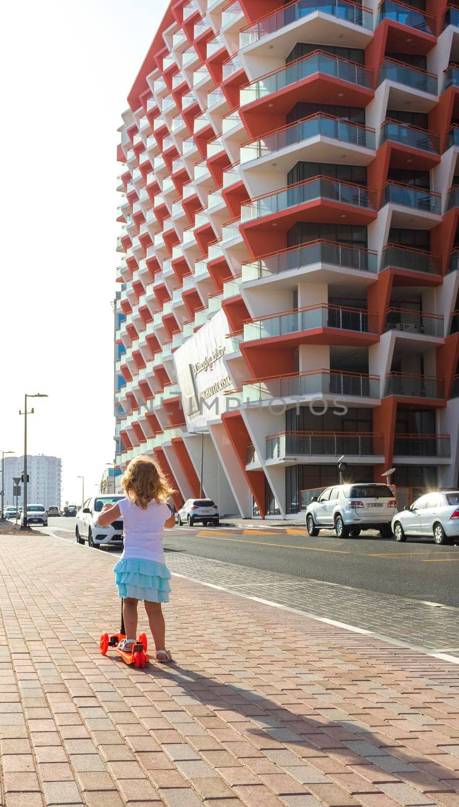 Dubai, UAE - 04.02.2021 - Little girl riding a scooter in front of Binghatti crystals residential building.