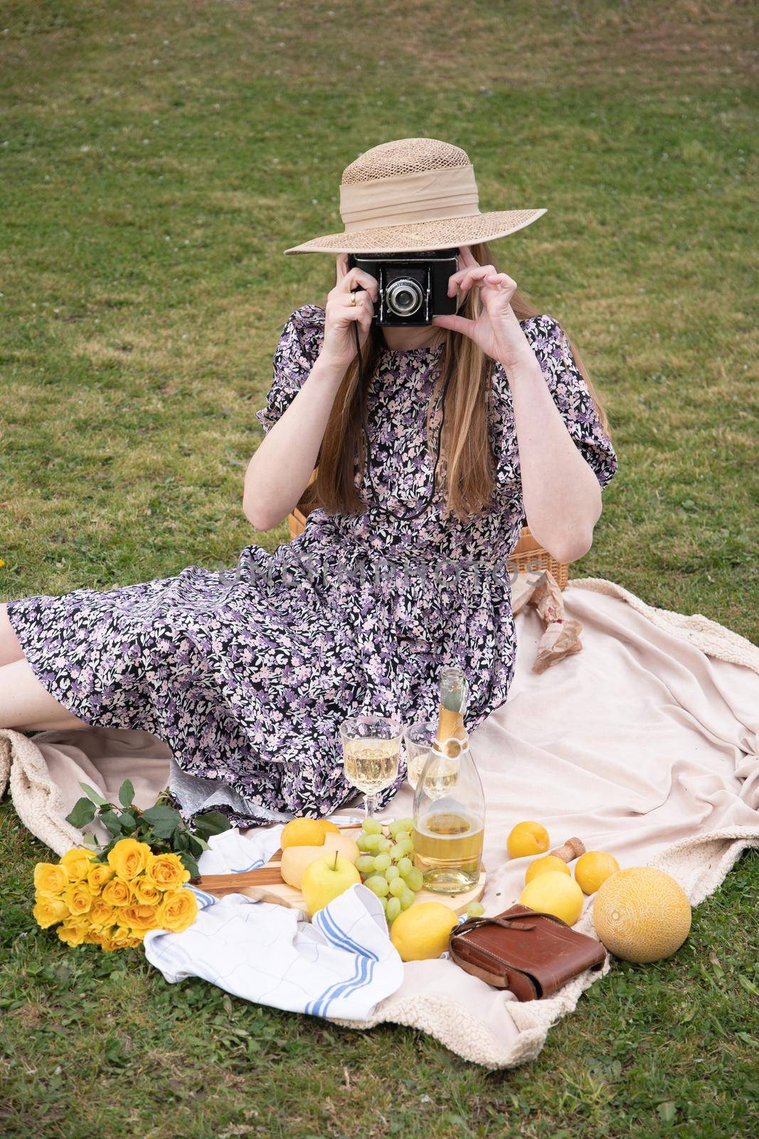 a young woman in a long dress and straw hat is resting on a picnic with fruits by KaterinaDalemans