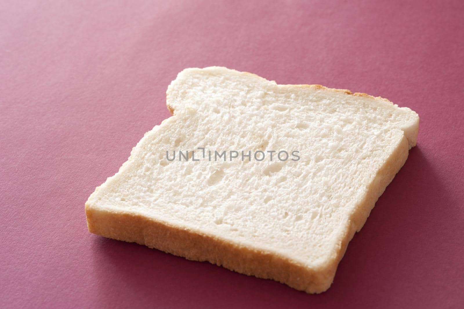 Slice of plain fresh white bread on a maroon background viewed low angle with copyspace