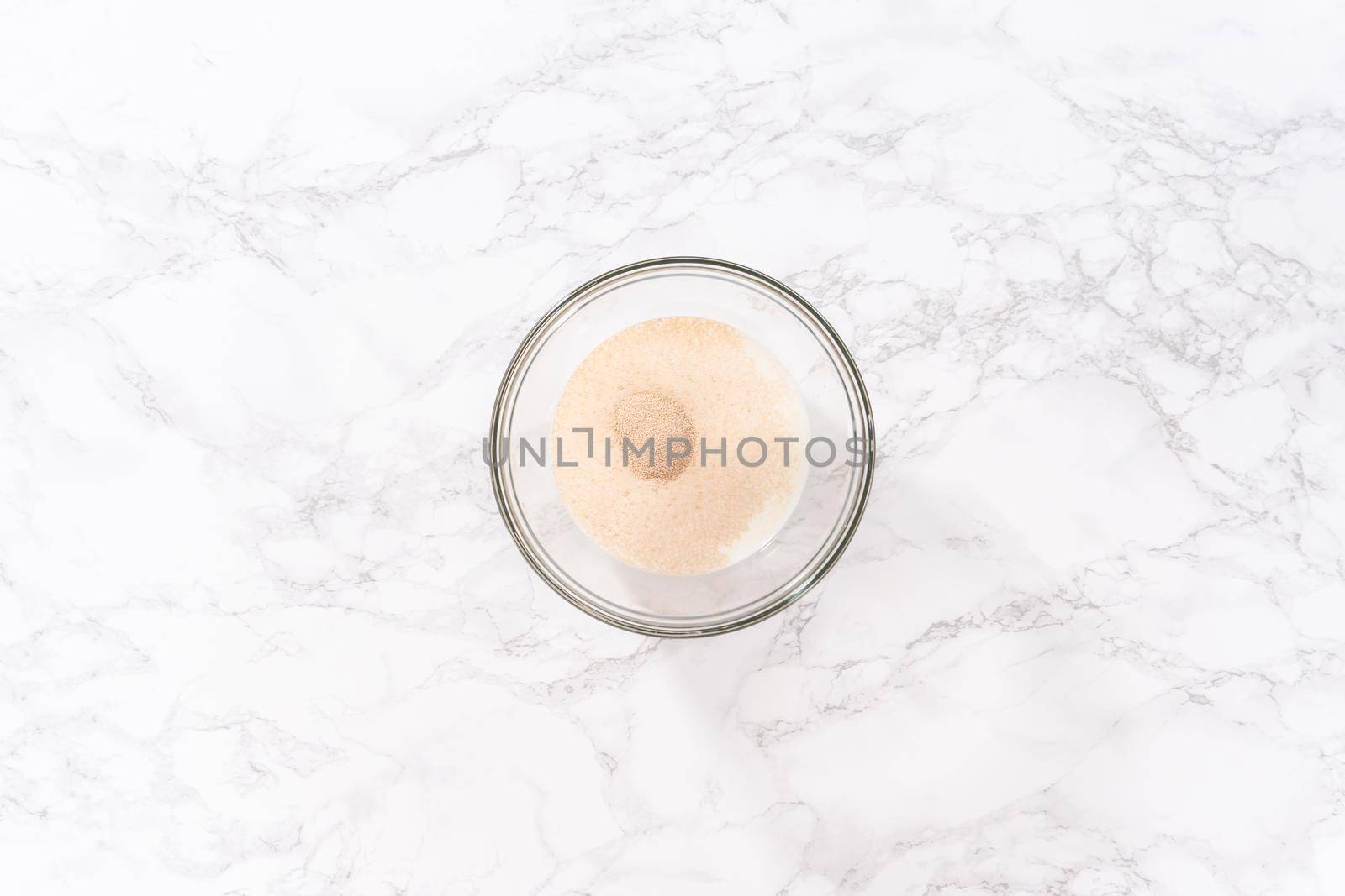 Flat lay. Activating dry yeast in a glass mixing bowl to prepare dinner rolls.