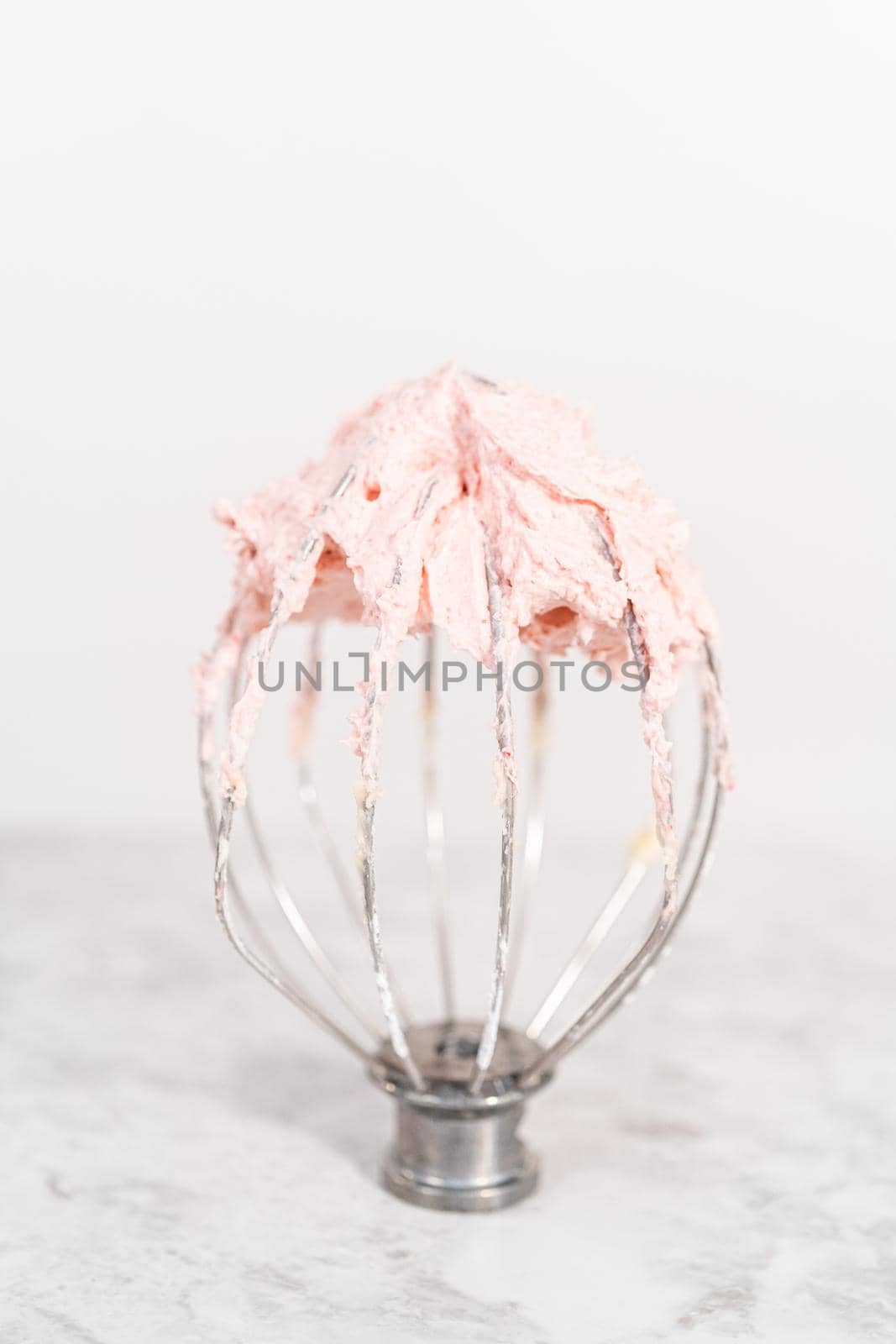 Whisk from the stang-along kitchen mixer filled with strawberry buttercream frosting.