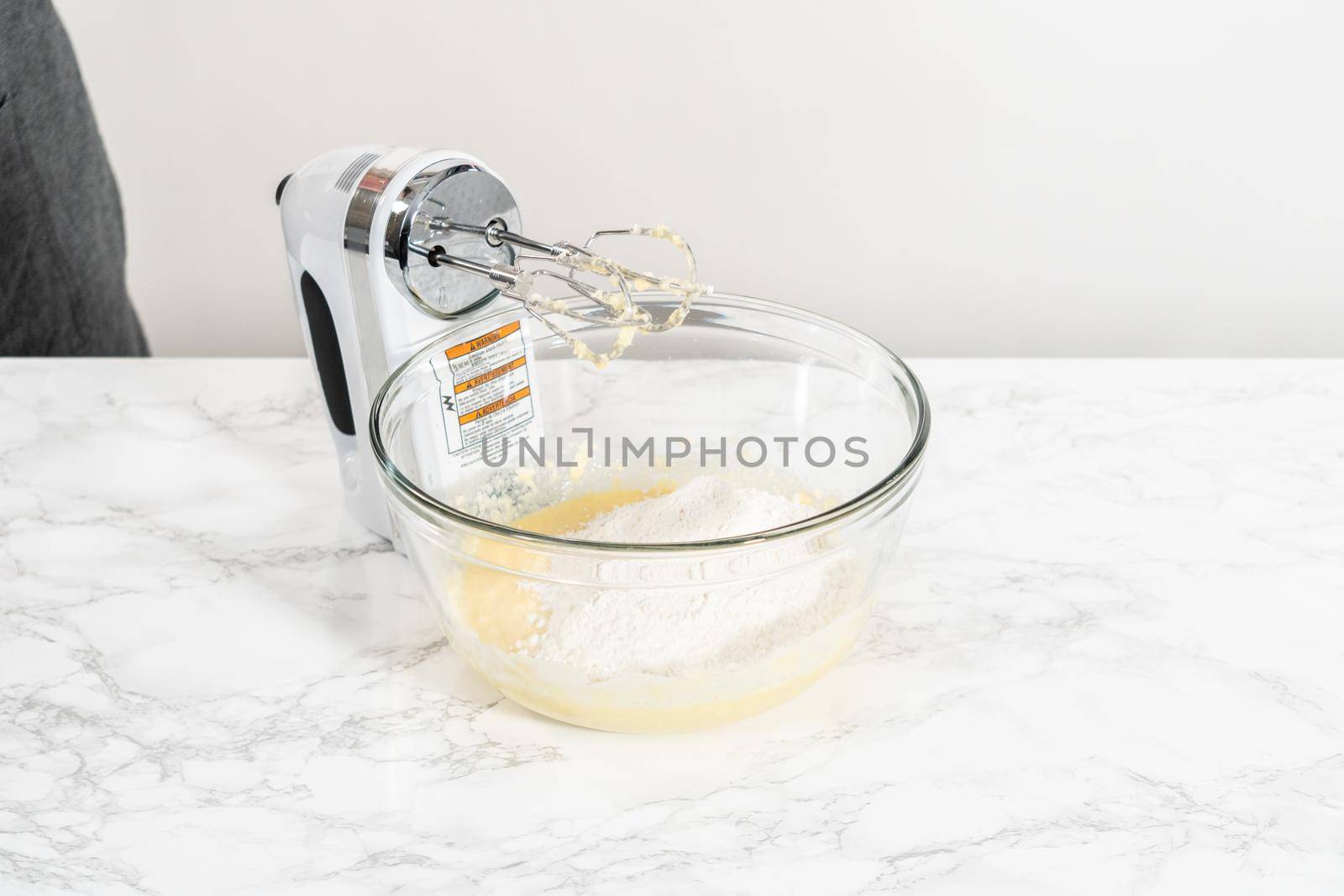 Mixing ingredients with a hand mixer in a large mixing bowl to bake mini vanilla cupcakes with ombre pink buttercream frosting.