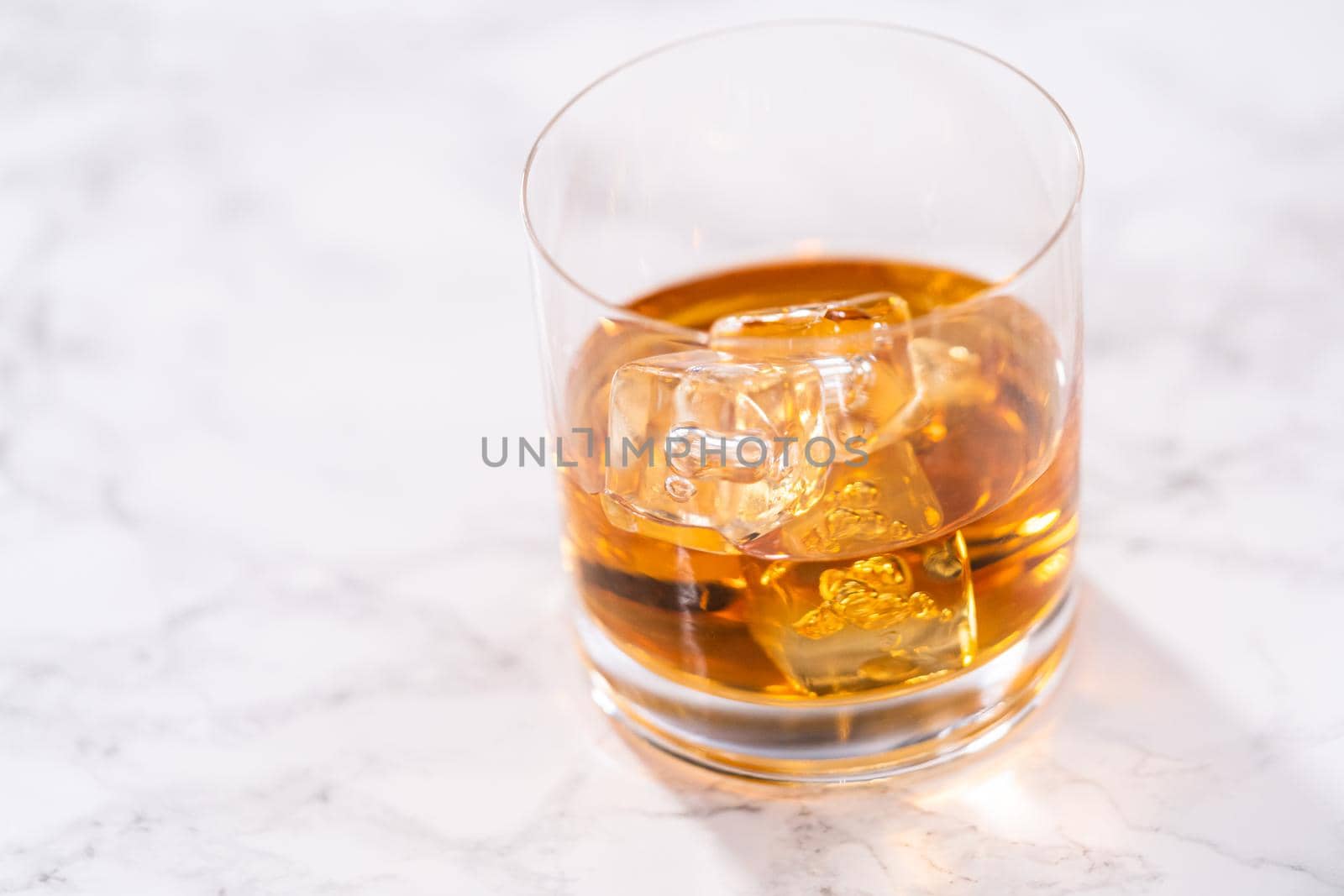 Scotch on the rocks in whiskey glass on a white marble surface.