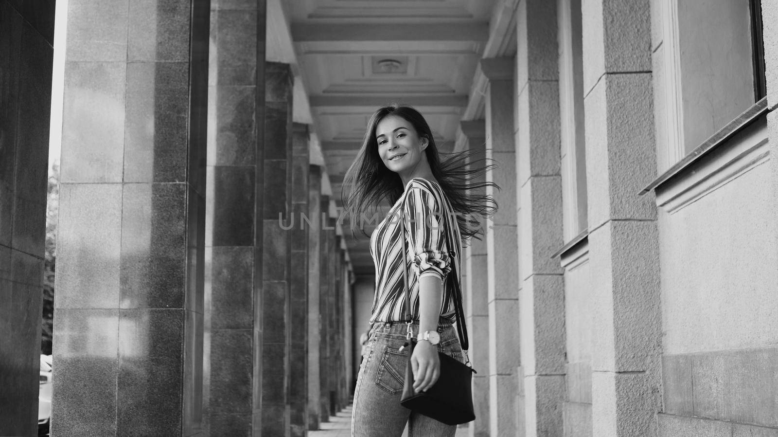 Street Style Outdoors Portrait of Beautiful Girl. Young Woman Smiling. Happy girl wearing Print Shirt, Jeans and Black Bag. Black and white shoot