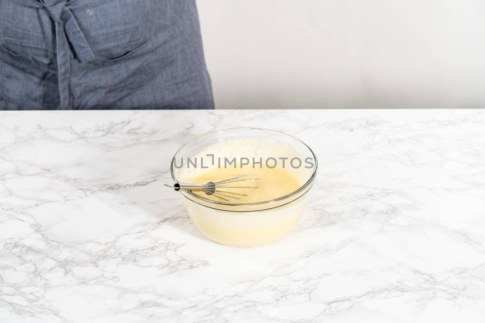 Mixing wet ingredients in a large glass mixing bowl to bake red velvet cupcakes with white chocolate ganache frosting.