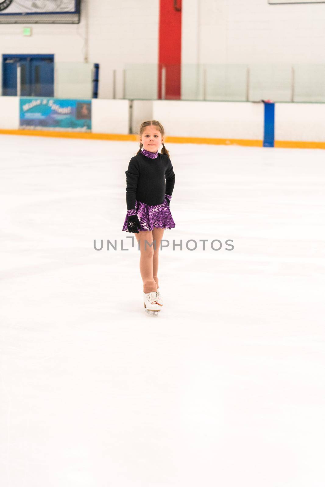 Little girl practicing figure skating on indoor ice skating rink.