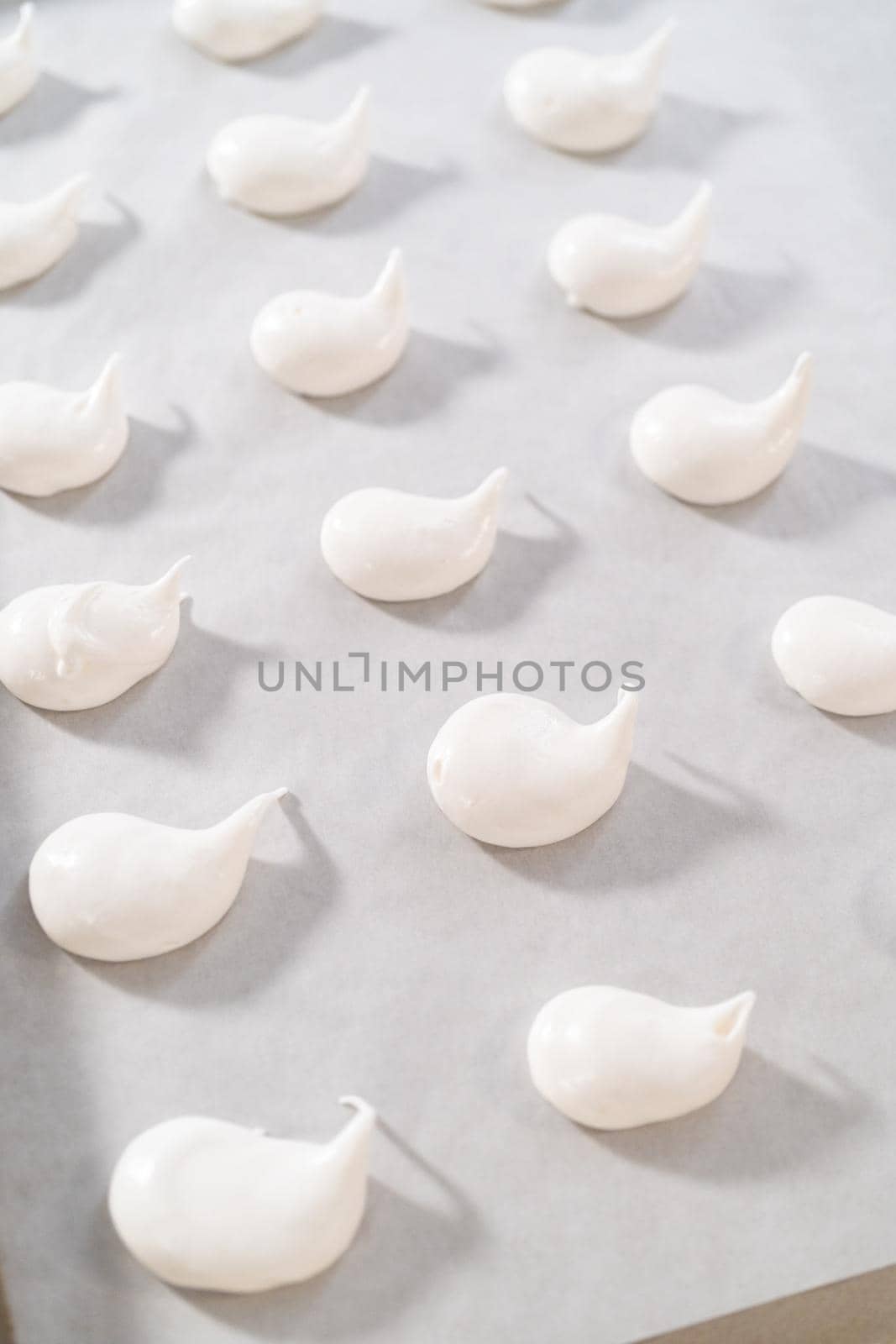 Piping meringue with piping bags into the baking sheet lined with parchment paper to bake Easter meringue cookies.