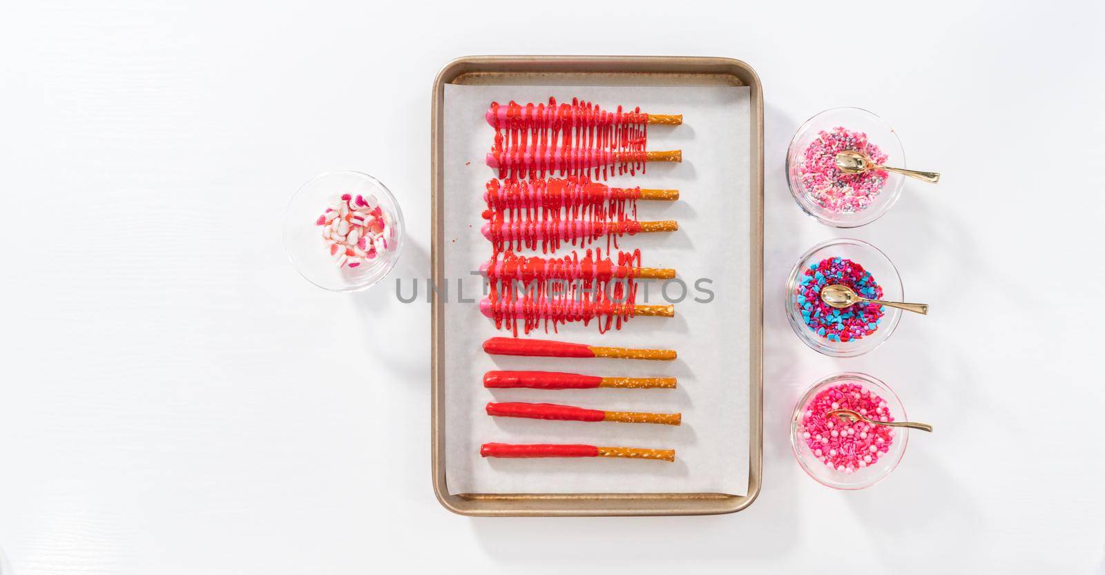 Flat lay. Drizzling melted chocolate over chocolate-dipped pretzels rods and decorating with sprinkles to make chocolate-covered pretzel rods for Valentine's Day.