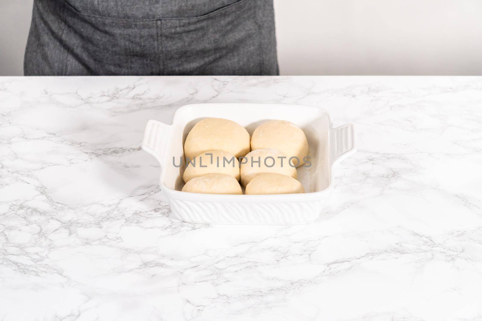 Rising dough in a white ceramic dish to prepare dinner rolls.