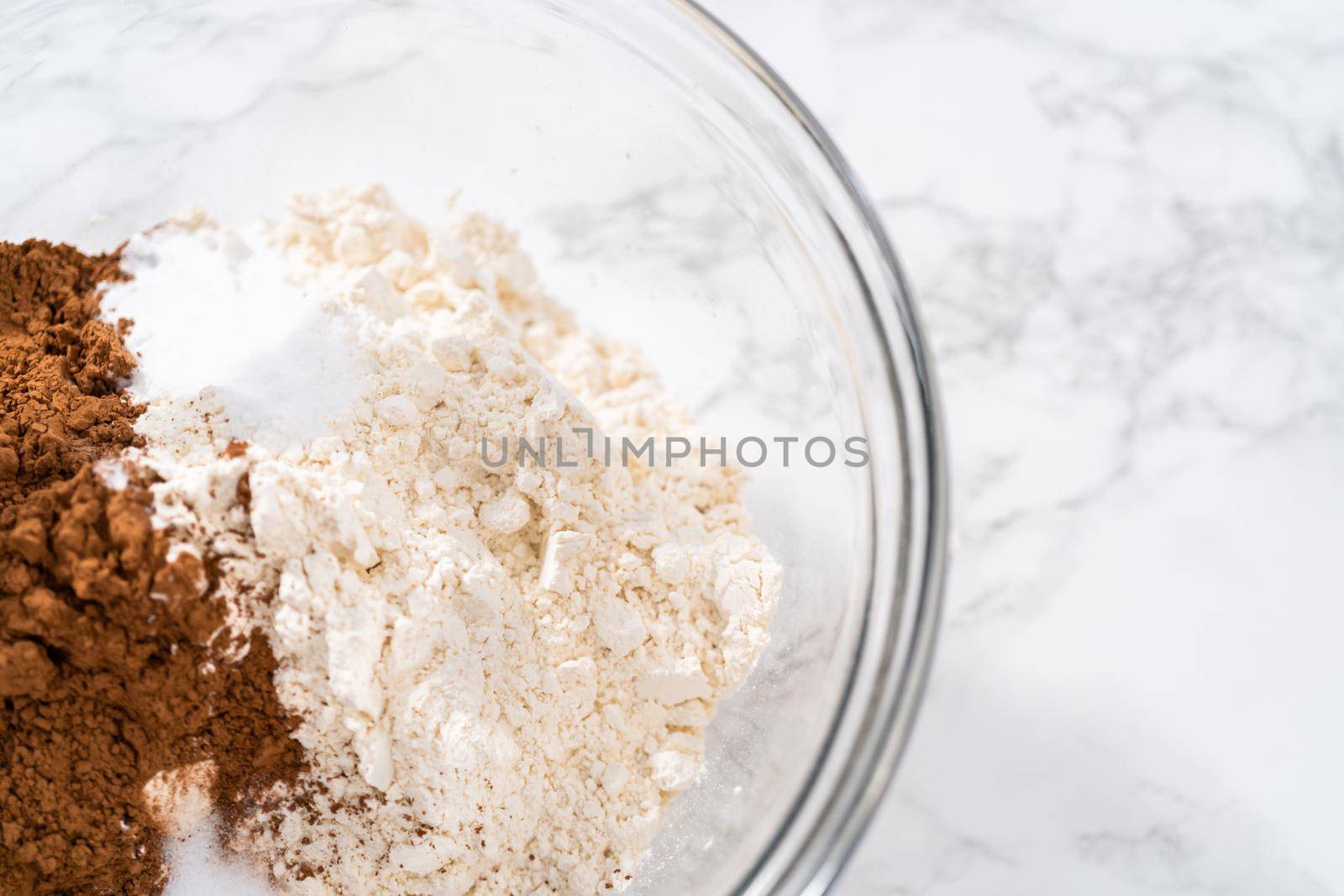 Mixing wet ingredients in a large glass mixing bowl to bake red velvet cupcakes with white chocolate ganache frosting.