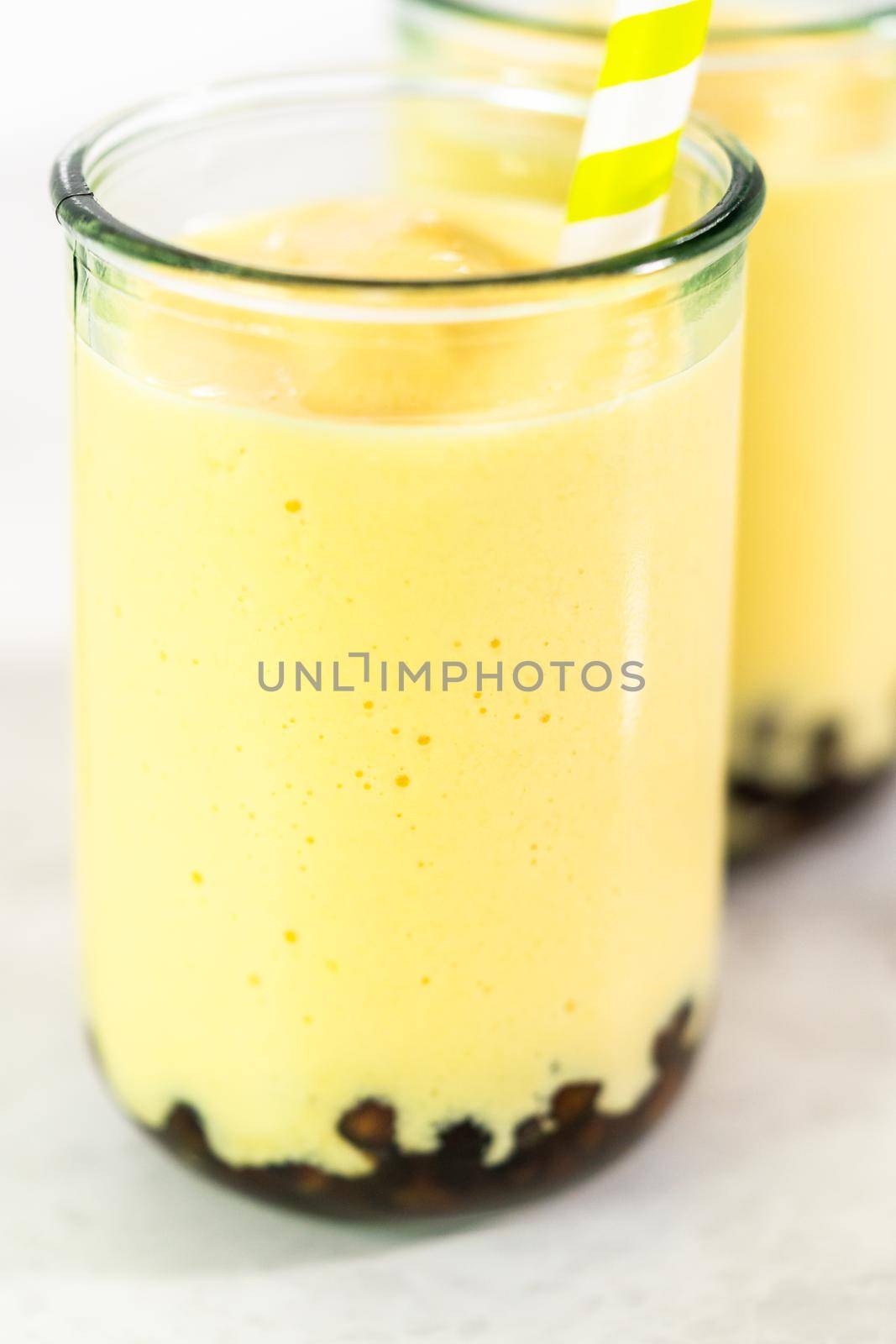 Freshly made mango boba smoothie in a drinking glass with a paper straw.