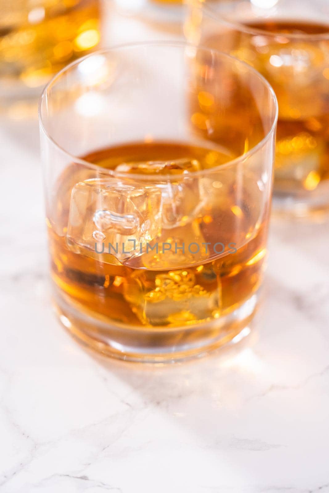 Scotch on the rocks in whiskey glass on a white marble surface.