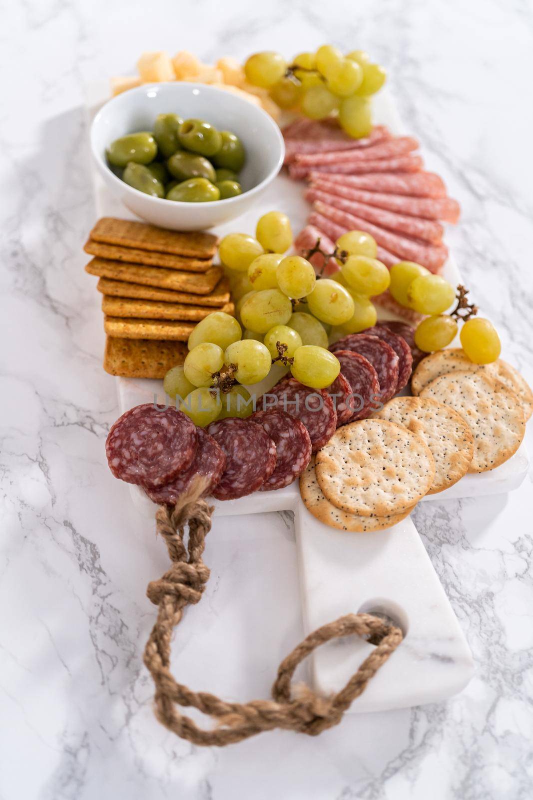 Cheese, meat, and crackers appetizer board on a marble surface.