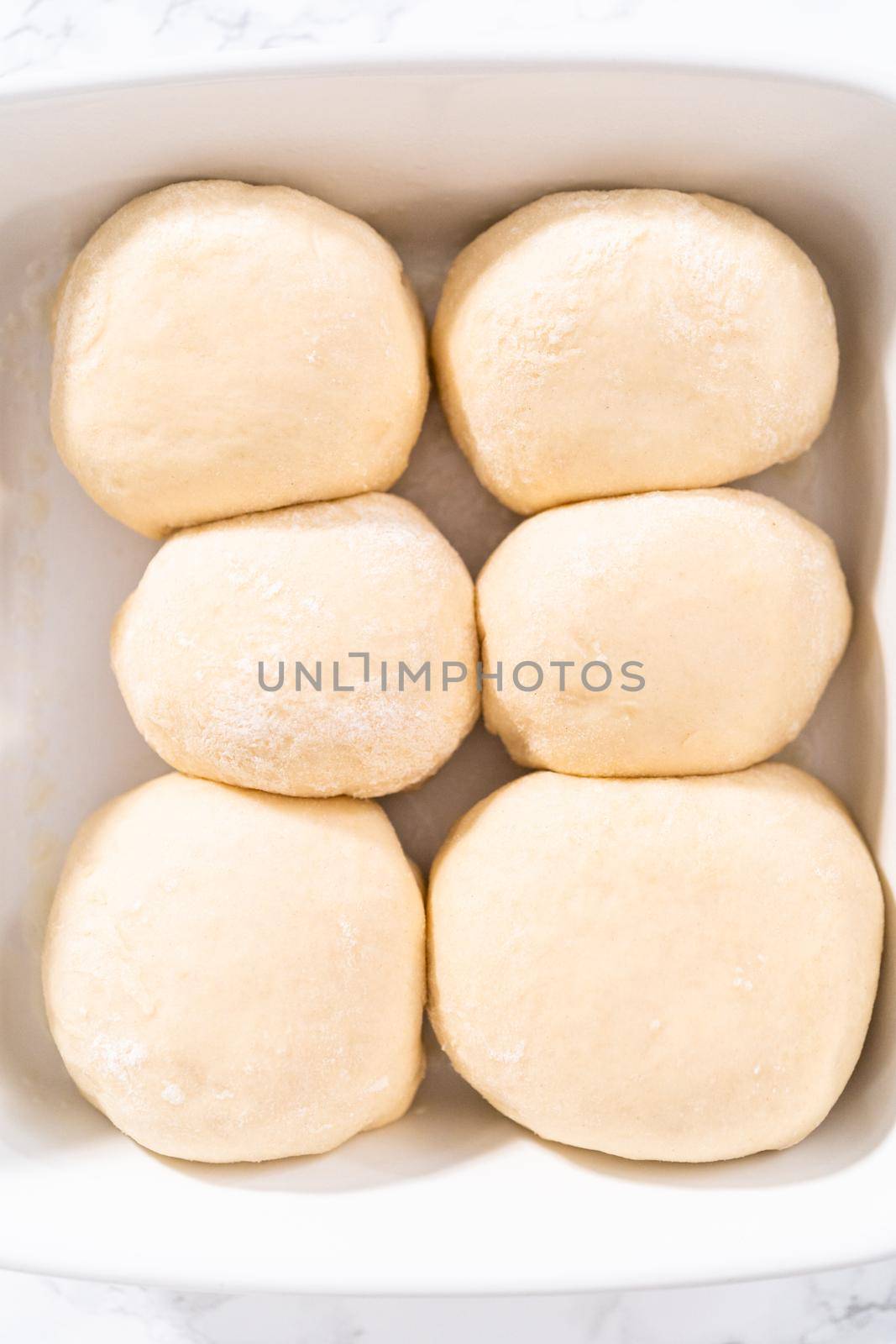 Rising dough in a white ceramic dish to prepare dinner rolls.