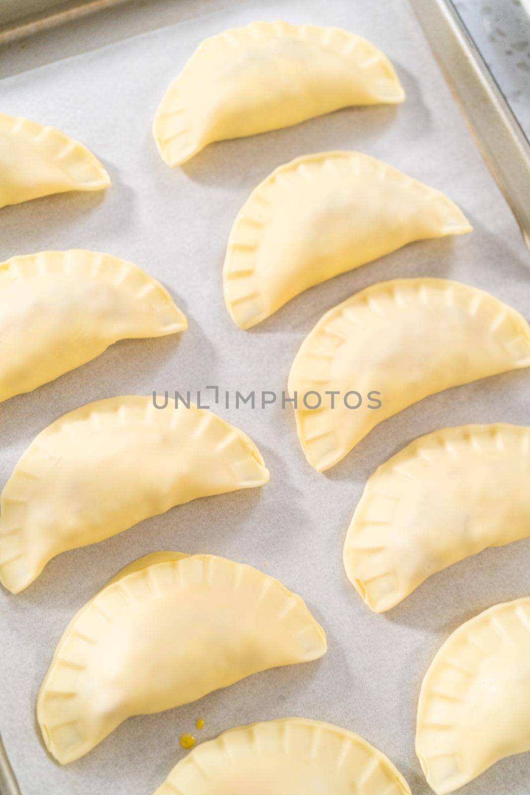 Brushing uncooked breakfast empanadas with eggs and sweet potato with egg wash.