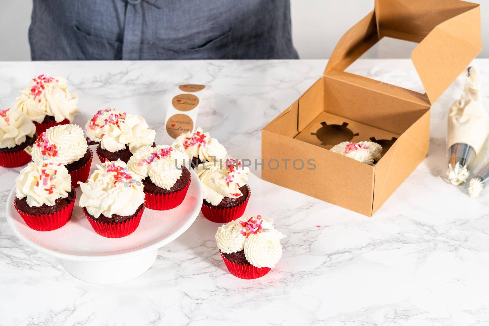 Packaging freshly baked red velvet cupcakes with white chocolate ganache frosting into the cupcake box.