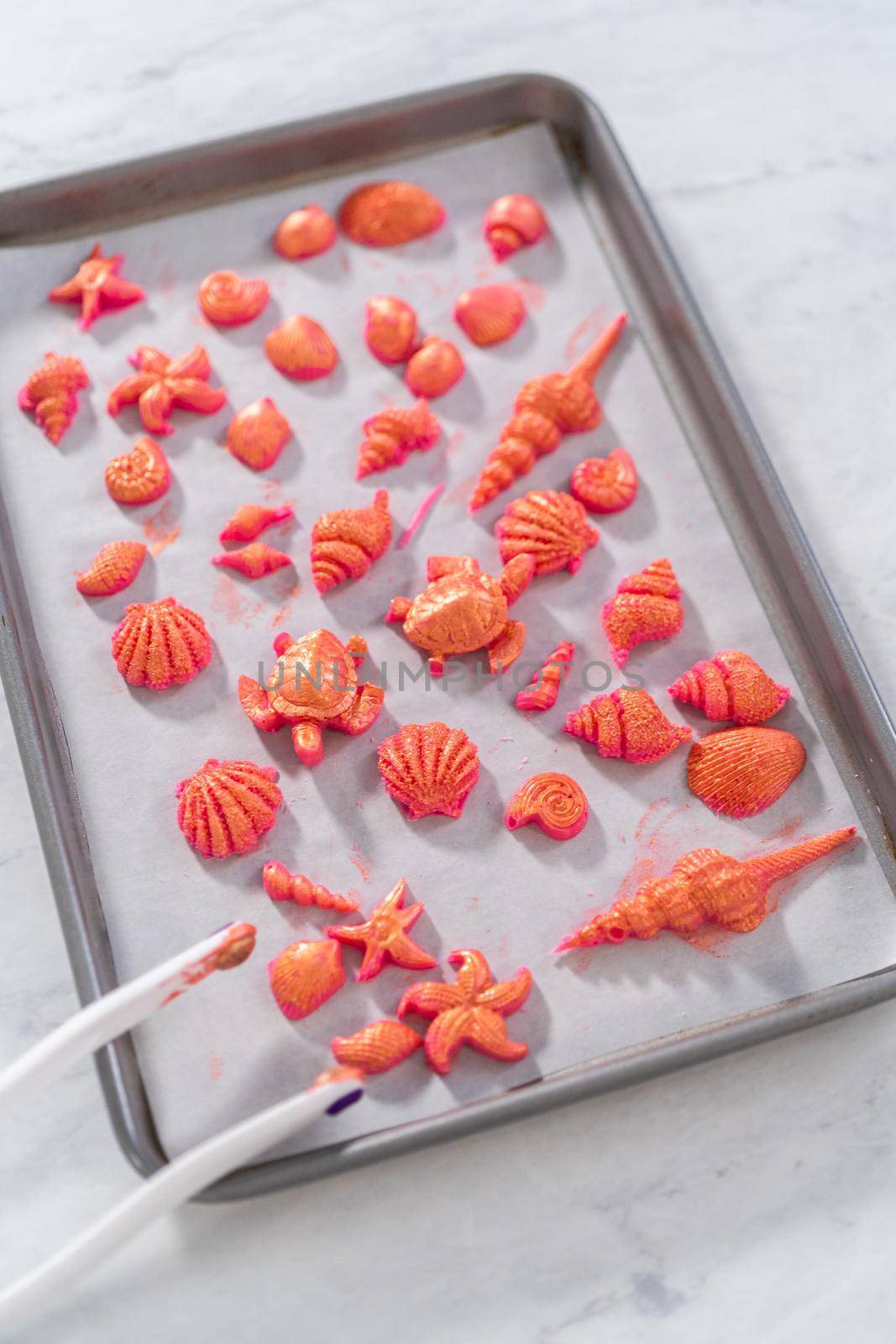 Painting sea-shaped chocolates with glittery luster to decorate chocolate-dipped pretzels twists.