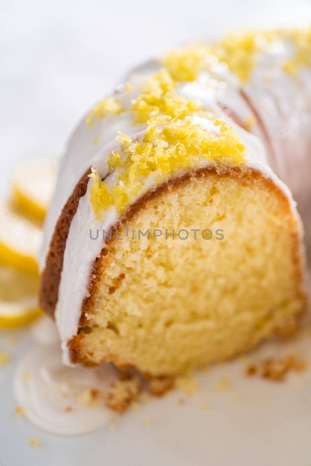 Sliced lemon bundt cake decorated with lemon zest on a cake stand.