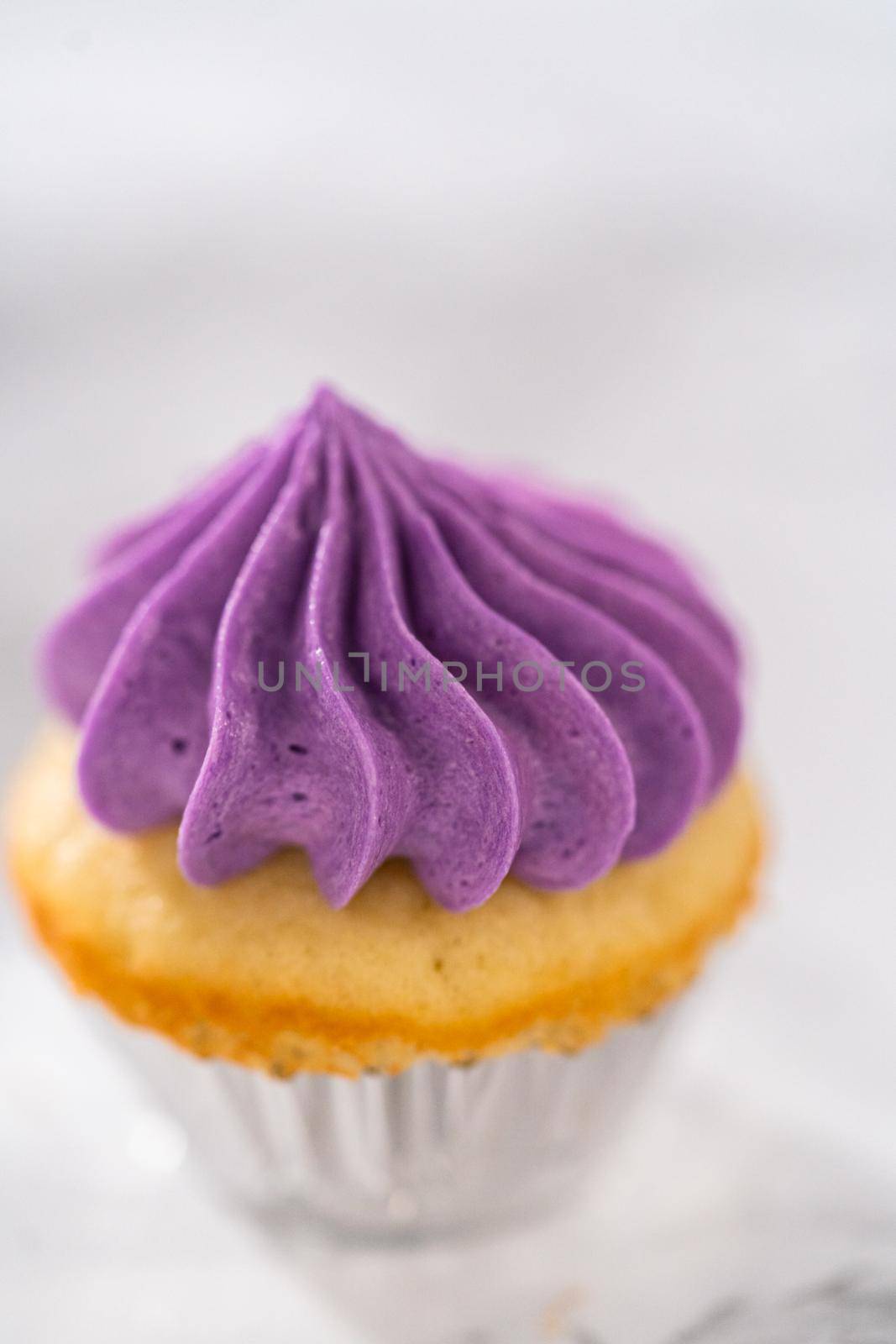 Freshly baked mini vanilla cupcakes with ombre pink buttercream frosting on a marble kitchen ocunter.