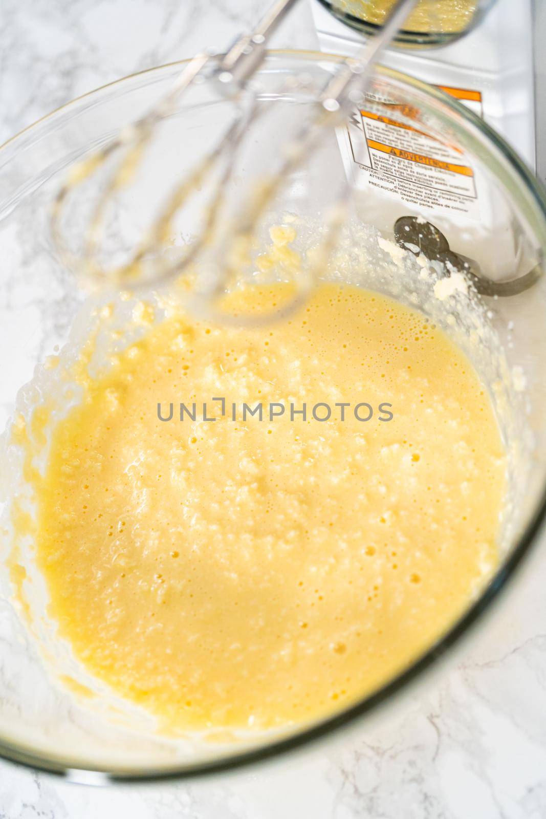 Mixing ingredients with a hand mixer in a large mixing bowl to bake mini vanilla cupcakes with ombre pink buttercream frosting.